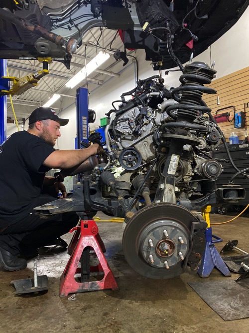 A mechanic performed auto repair services under a vehicle with the subframe and engine removed at Collinsville Auto in Canton, CT