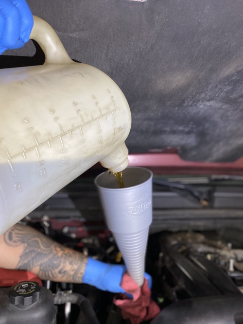 A mechanic pours new oil into an engine while performing an oil change at Collinsville Auto