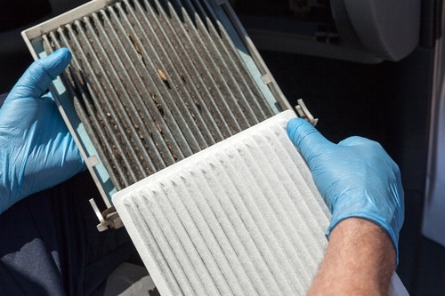A mechanic holds up a dirty cabin air filter next to it's new counterpart