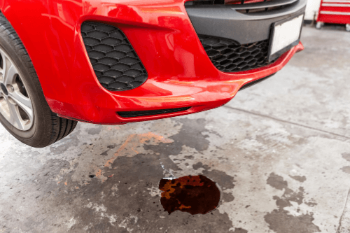 How to tell when it is time to service your car with Collinsville Auto Canton, Ct. red sedan on lift in shop with a puddle of fluid underneath due to a leak