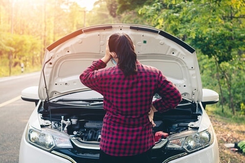 Collinsville Auto: What is a BG Flush? in Canton, CT; image of brunette woman wearing red plaid flannel shirt facing car engine with hood open holding her left hand on her head as her car is broke down on the side of the road