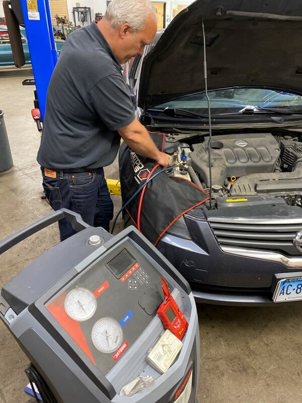 Collinsville Auto Repair owner using A/C testing machine to test blue nissan sedan car to see if A/C is working properly