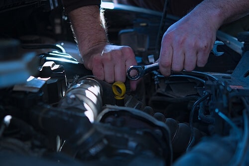 Engine Repair in Canton, CT | Collinsville Auto Repair. Closeup image of an auto mechanic working on a car engine in a car garage.