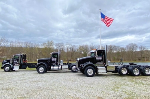 Collinsville Transport Services in Canton CT, image of their 3 transport trucks parked next to each other with a tall flagpole behind them with the American Flag attached