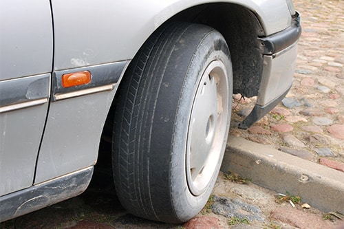 Collinsville Auto Repair| Car with worn tire tread on front wheel is parked in the street of Canton, CT,.