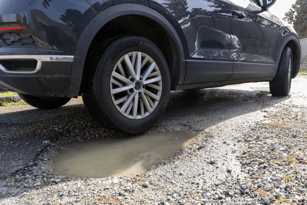 Suspension repair, auto repair in Canton, CT by Collinsville Auto Repair. Image of an SUV tire near a deep pothole, highlighting risks of wheel damage, misalignment, and the need for professional suspension and tire inspections for safe driving.
